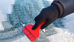 person using ice scraper on windshield of vehicle