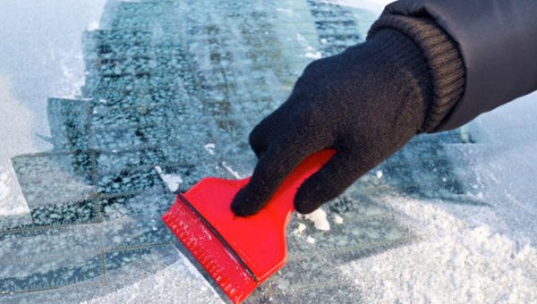 person using ice scraper on windshield of vehicle