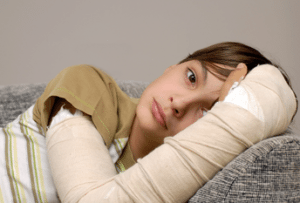 Adolescent girl with a bandaged broken arm laying on a sofa