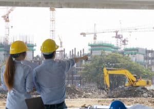 Man and woman with yellow hard helmets strategizing on a construction site looking at an earth mover