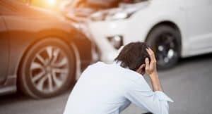 Man holding head after a car accident with cars in the background