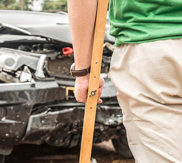 Man on crutches standing in front of car with damage on the front