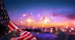 Usa Celebration With Hands Holding Sparklers And American Flag At Sunset With Fireworks