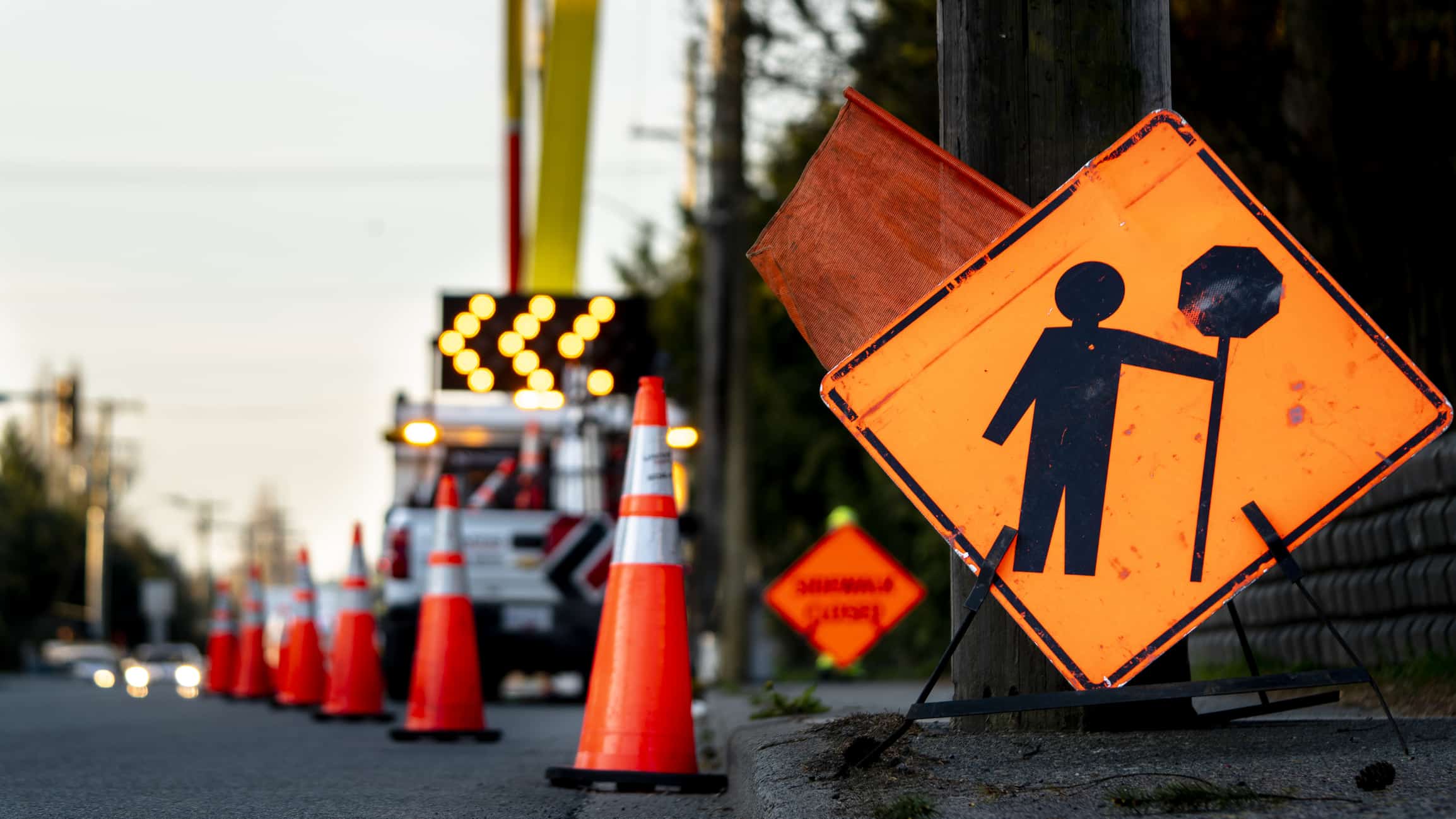 Lane closure on a busy road due to maintenance signs detour traffic temporary street work orange lighted arrow, barrels, and cones.