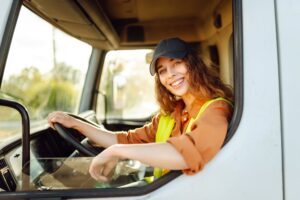 A young woman sits in the cab of a truck and smiles because she knows the answer to the question: What are regulations for truck drivers in Wisconsin?