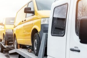 A tow truck carries a yellow van minibus away from a crash scene. You should get medical help and then talk with a lawyer about recovering personal injury damages after an accident with a DHL truck.