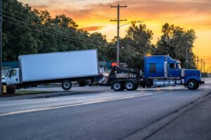 A tow truck carries a broken semi-truck tractor away from an accident scene. If a FedEx truck runs into you on the road, get medical help and consult a lawyer to learn how you can recover accident damages.