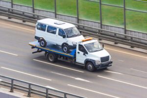 A platform tow truck carries a small van down a street. If a UPS truck runs into you on the road, get medical aid and talk with a lawyer about how you can recover accident damages.